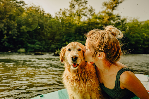 Photo of a young woman kissing her dog while paddling on a river; enjoying the beautiful, warm summer afternoon far from the hustle of the city.