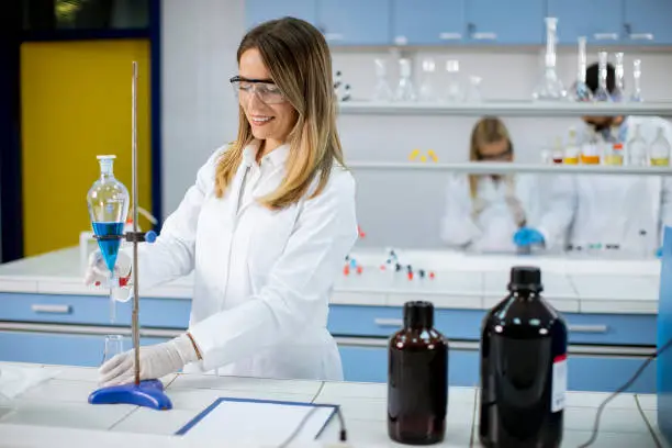 Photo of Young female researcher working with blue liquid at separatory funnel