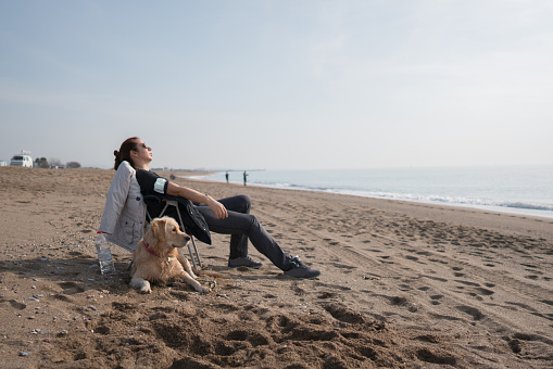 Woman sitting  with her dog on beach.