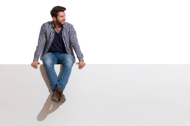 sonriente hombre guapo está sentado en una parte superior de bandera blanca y mirando a un lado - lumberjack shirt fotografías e imágenes de stock