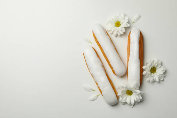 Delicious eclairs with custard and chamomiles on white background