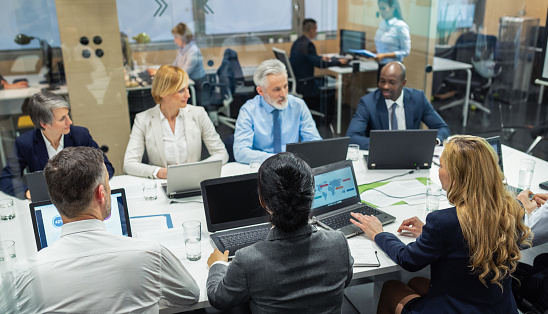 Serious diverse business colleagues discussing work paper documents on meeting, bending over table with sales reports. Different aged business team brainstorming on marketing strategy, analysis