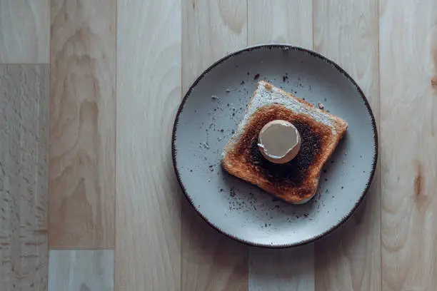 Empty boiled egg shell on burnt toast surrounded by crumbs on a plate in a conceptual image