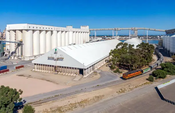 Wide angle view from drone of a diesel locomotive unloading grain at the Port grain terminal. The train is dwarfed by the huge grain storage facility and conveyor system. The Port River can be seen in the background. All logos and ID have been removed.