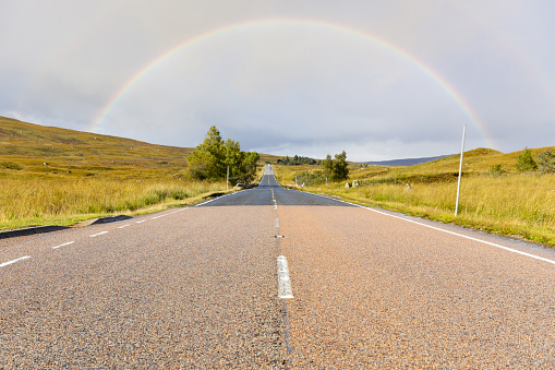 Empty road in the highlands, Scotland, leading to a rainbow - Travel and transportation concept with Scottish landscape on background near Glencoe