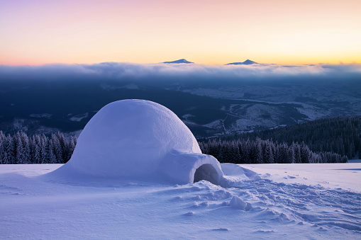 Igloo the house of isolated tourist is standing on high mountain far away from the human eye. Amazing winter sunrise. Marvelous huge white snowy hut. Nature landscape.