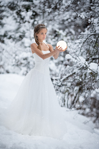 Beautiful woman in a white snow crystal dress holding the full moon in her hands. Snow flakes falling from the sky on this cold winter day. Nikon D850. Converted from RAW.