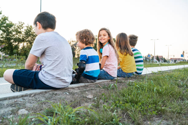 Two kids sitting on a small wooden bridge near a stream, surrounded by tall grass and stones. Summer outdoor childhood, nature exploration and family adventure.