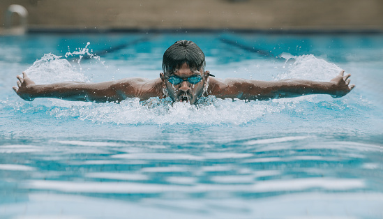 Asian indian swimmer swimming and practicing in swimming pool with butterfly style