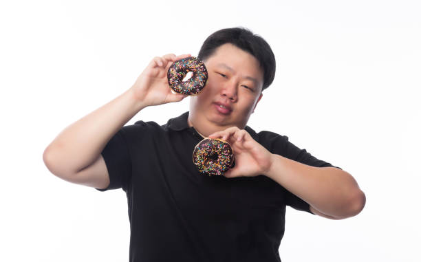 istock Young Funny Fat Asian man playing with chocolate donuts isolated on white background, Unhealthy concept 1295469424