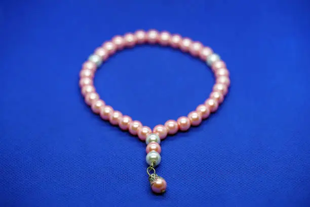 silver and pink beaded tasbih or tasbeeh isolated on blue background.
