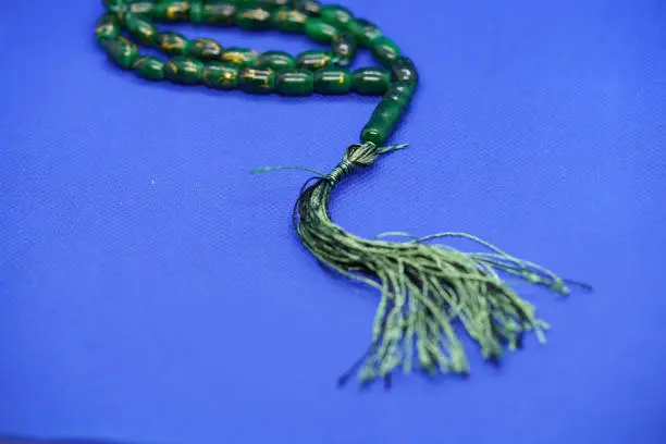 Green tasbih or tasbeeh yarn isolated with blue background.