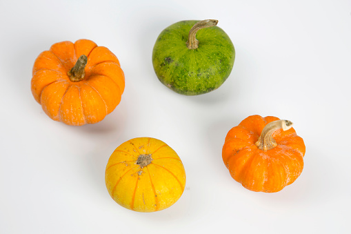 Small pumpkins of different colors isolated on white background. Foods, fresh vegetables, recipe, Halloween and Thanksgiving concepts. Horizontal close-up, top view.