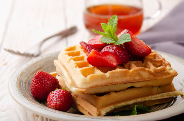 de mening van de close-up bij belgische wafels die met aardbeien en muntblad op witte houten keukenlijst met stroop terzijde worden geserveerd - stroopwafel stockfoto's en -beelden