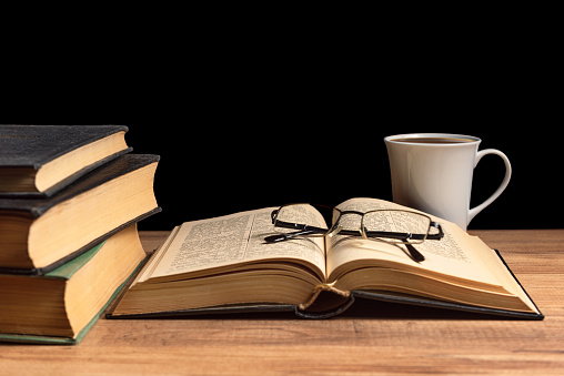 Open old book, coffee and glasses on the table.
