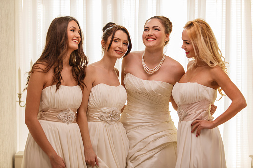 Front view of beautiful young bride standing embraced by three of her bridesmaids in beautiful white dresses.