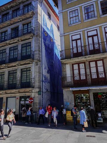 Porto, Porto, Portugal- June 13, 2019: Pedestrians and shoppers on a downtown Porto, Portugal street. A large wall mural of a blue cat is visible in a side alley.