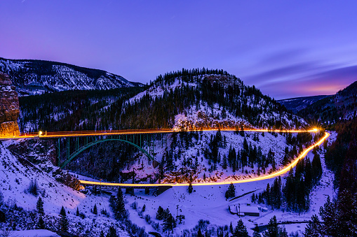 Red Cliff Colorado Winter Views - Town and iconic bridge glowing at dusk time exposure with cars creating light trails. Scenic wide angle view with Highway 24 looking south to Leadville, Colorado and Tennessee Pass.