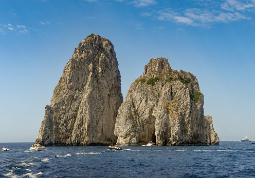 Wide angle view of the Faraglioni rock formation off the coast of Capri. Small boats are passing through the arch.
