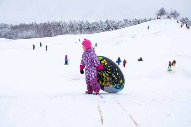 ein kind, ein 5-jähriges kaukasisches mädchen, hat spaß auf den schneebedeckten bergen, steigt den berg hinauf, um auf einem aufblasbaren ring zu rutschen. - child winter snow 4 5 years stock-fotos und bilder