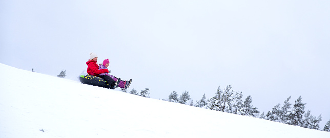 A family of Caucasians on a winter weekend vacation. Young woman with a baby boy 5 years old. They have fun on snow-covered slides, slide on an inflatable ring.