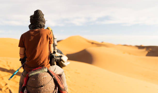 impresionante vista de dos personas montando camellos en las dunas de arena en merzouga, marruecos. - camel ride fotografías e imágenes de stock