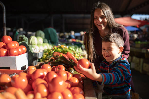 un ragazzo carino che raccoglie verdure con sua madre - farmers market foto e immagini stock