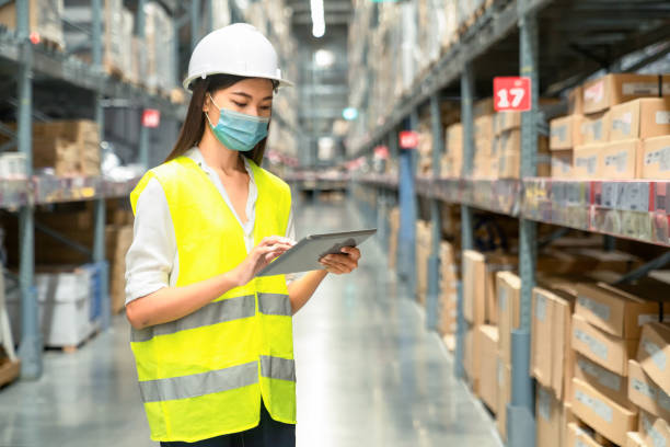 verticale de travailleur asiatique d’entrepôt restant dans le grand centre de distribution d’entrepôt avec la tablette numérique. dans les étagères de fond avec des marchandises. - data center computer programmer women photos et images de collection