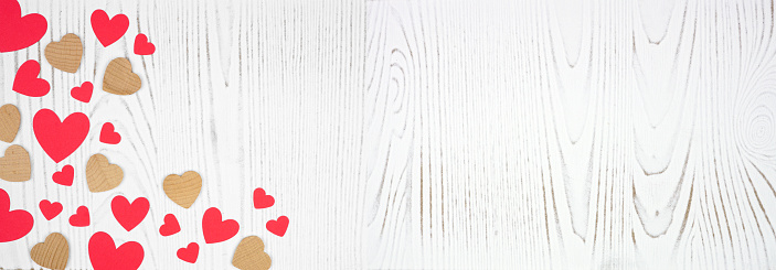 Valentines Day banner with corner border of red and wood hearts. Top down view on a white wood background. Copy space.
