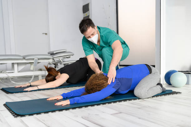 donna che si allena con terapista su tappetino yoga in clinica. foto di alta qualità - yoga men male gymnastics foto e immagini stock