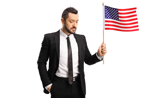 Upset young businessman holding a USA flag and looking down isolated on white background
