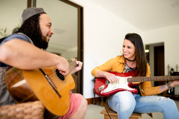 istock Two smiling young friends playing guitar together at home 1295509577