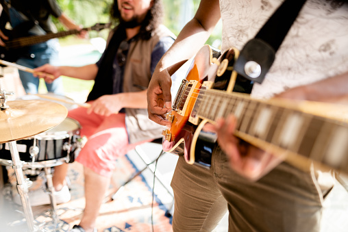 Close-up of a young man playing an electric guitar during a jam session with his band in a home studio