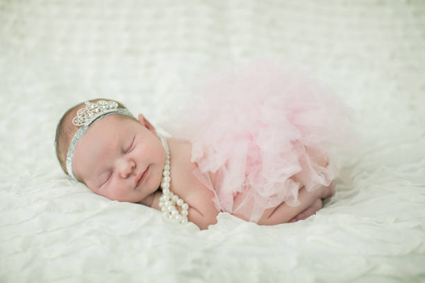nahaufnahme eines süßen neugeborenen baby-baby-mädchen auf einem cremefarbenen neutralen hintergrund mit einer krone auf dem kopf wie eine kleine prinzessin royalty. - royal baby stock-fotos und bilder
