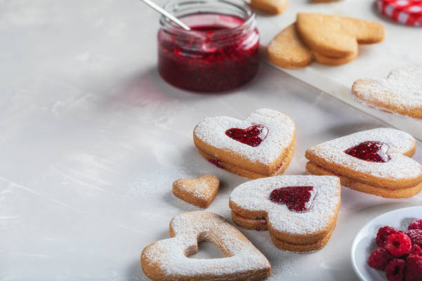 istock Heart-shaped cookies with raspberry jam on light gray background with copy space. Valentine's Day or Christmas biscuits making process. 1295520500