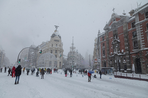 Madrid, Spain - January 09, 2021: Pedestrians and people walking in front of the Metropolis building between Alcala street and Gran Via, on a snowy day, due to the Filomena polar cold front.