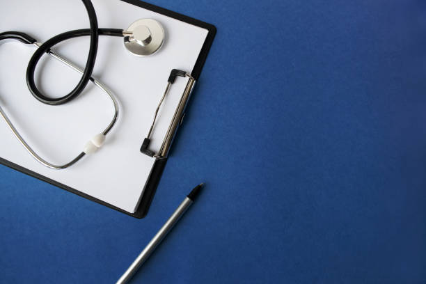 istock Doctor's workplace. Top view on a blue background with medical equipment - stethoscope, tablet with a blank sheet of paper, glasses. Medical concept. 1295525158