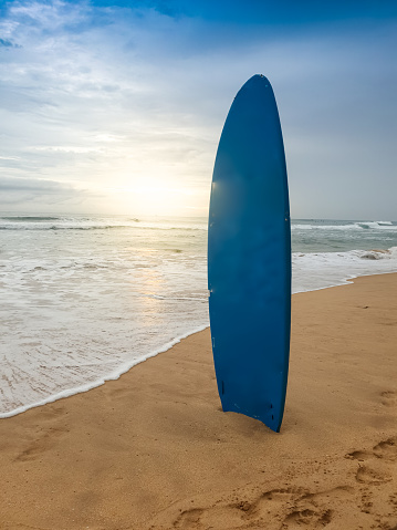 Beautfiul photo of blue surboard standing on sandy ocean beach at sunset