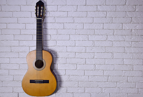 An acoustic guitar stands upright against a light brick wall on the left side. On the right, there is plenty of space for lettering, advertising or text