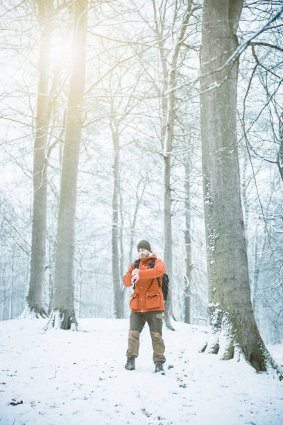 Male with knitted hat and orange winter jacket checking his health information and tracking GPS position on smart watch while hiking outdoors in a winter wonderland snow covered forest.  Wearable technology has boomed lately where social distancing due to Covid-19 opens the opportunity to spend more time in nature and focus on personal health. Wireless technology and the G4 and G5 network also facilitate theis new trend.