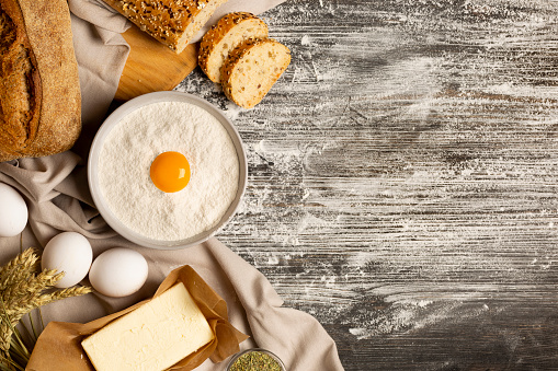 Top View Bakery Background with Freshly baked bread, Wheat, Wholegrain and seeds sliced bread, Bowl with Flour, Eggs, Butter, Olive Oil, Rolling Pin and Herbs