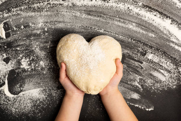 Baking Background. Heart shaped dough for bread with child hands and flour stock photo