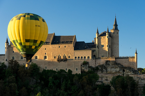 Segovia, Spain - October 05, 2019: View of the Alcazar fortress of segovia at sunrise with various hot air balloons in the sky, listed world Heritage centre by UNESCO
