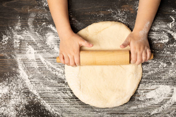 istock Child hands Rolling Dough with Rolling Pin on wooden table for homemade bakery 1295542345