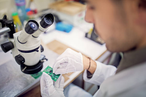 l’homme examine le circuit imprimé dans une usine - male magnifying glass caucasian technician photos et images de collection