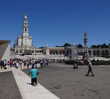 Fatima,Santarem, Portugal- June 9, 2019: Large square of Sanctuary of our Lady of Fatima church and pilgrimage site. Many people, some crawling on their knees to the final sanctuary.