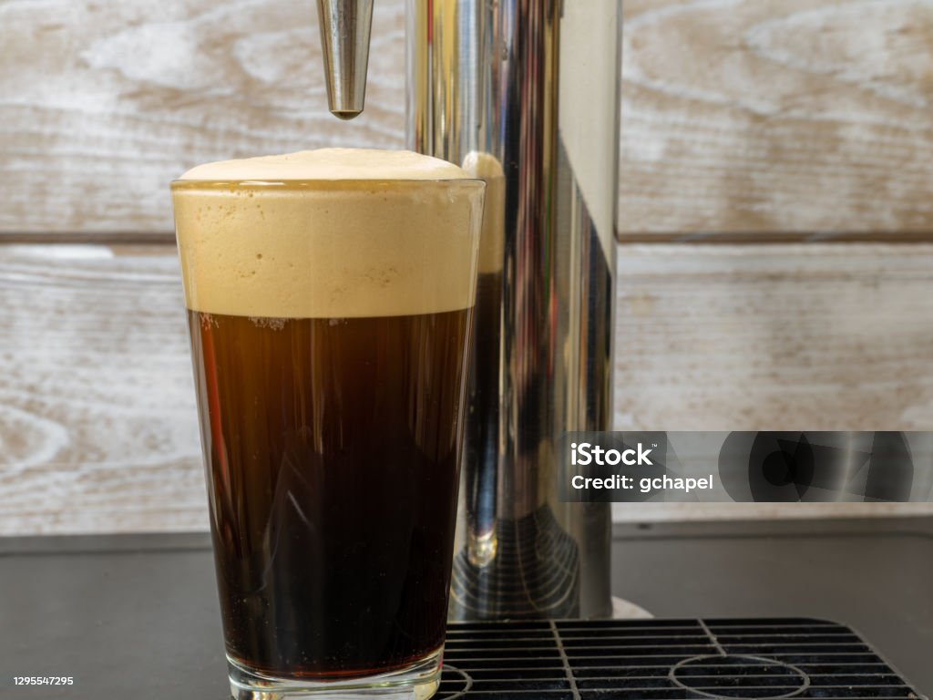 Nitro cold Brew Coffee in a clear glass on a dispenser Nitro Cold Brew coffee pouring into a clear glass with fine nitrogen bubbles and a smooth texture on a keg coffee dispenser. Cold Brew Coffee Stock Photo