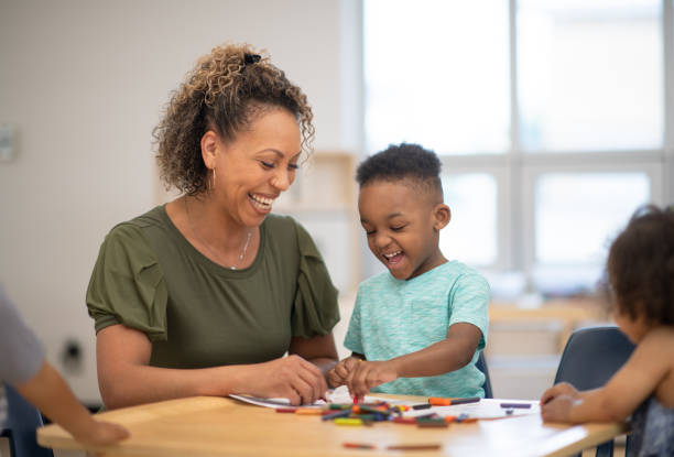 Colouring together is more fun A preschool teacher and her student are colouring together at a desk. They are both of African ethnicity. community center stock pictures, royalty-free photos & images