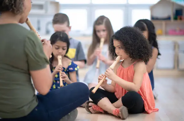 A multi ethnic group of preschool children are sitting on the floor and they each have a flute to use during music class.