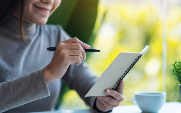 istock a beautiful young asian woman holding and writing on a notebook 1295562523